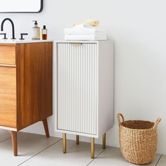 a white cabinet next to a sink and a basket on the floor in front of it