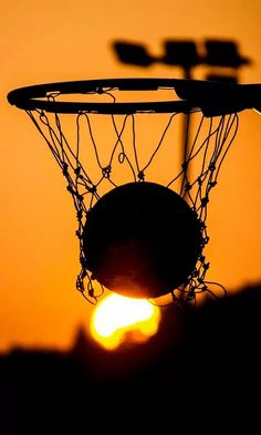 a basketball hoop with the sun setting in the backround behind it, as seen from below