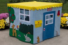 a child's play house in the middle of some flowers and grass with yellow trim