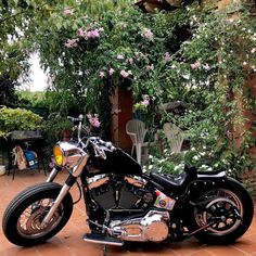 a black motorcycle parked on top of a red brick floor next to trees and flowers