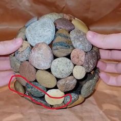 two hands are holding a rock ball made out of rocks and red string on the bottom