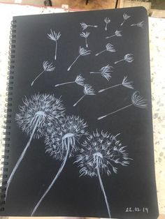 a drawing of a dandelion blowing in the wind on a black paper notebook