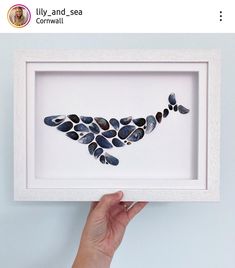 a hand holding up a framed artwork with rocks in it's shape and the words lily and sea on it