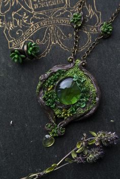 a necklace with green and purple flowers on it, surrounded by other jewelry items including an oval shaped pendant