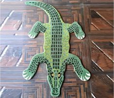 a green crocheted alligator laying on top of a wooden floor next to a wall