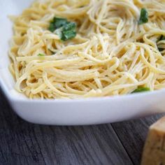 a white bowl filled with pasta and spinach on top of a wooden table next to two slices of bread