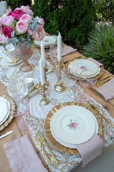 the table is set with white and gold plates, silverware, pink flowers and candles