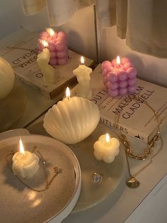 some candles are sitting on a table next to books and other items that include seashells