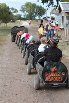 several children are riding on small carts down the dirt road while others watch from behind them