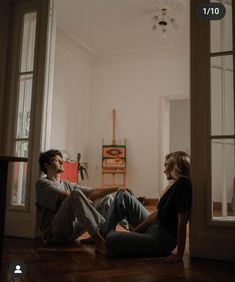 two people sitting on the floor in front of an open door and looking at each other