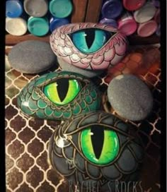 painted rocks with green and blue eyes are on a patterned surface next to other rocks