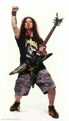 a man with long hair holding a guitar in his right hand and wearing camo shorts