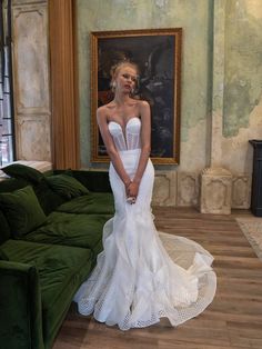 a woman in a white wedding dress standing next to a green couch and painting on the wall