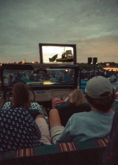 three people sitting in the back of a truck watching a movie