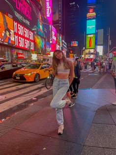 a woman is walking down the street in times square, new york city at night