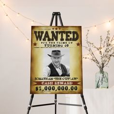 a wanted poster on an easel next to a vase with flowers and string lights