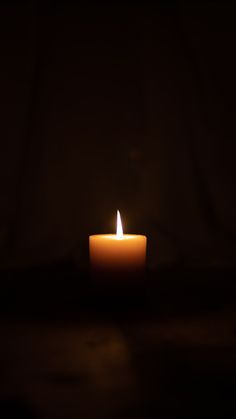 a lit candle sitting on top of a table in the dark with only one burning