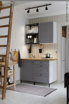 a kitchen with grey cupboards and wooden stairs in the corner, along with a ladder leading up to it