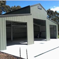 an empty garage with two doors open in front of some trees and grass on the ground