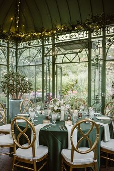 a dining room with green table cloths and gold chairs in front of a glass wall