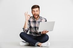 a man sitting on the floor with his laptop in front of him and making an ok sign