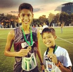 two young boys standing next to each other on a soccer field with medals around their necks