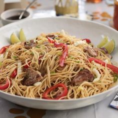 a white bowl filled with noodles and meat on top of a table next to drinks