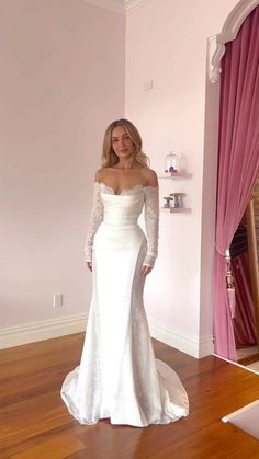 a woman in a white wedding dress standing on a wooden floor next to a pink wall