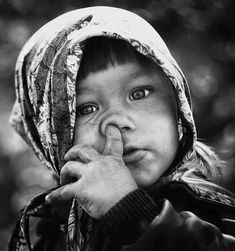 a young child with a hood on holding his finger to his nose and looking at the camera