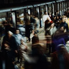 a crowd of people walking down a street next to a subway train at night time