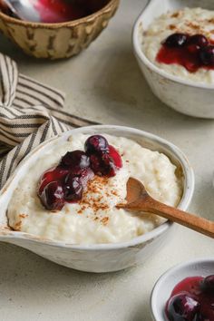 two bowls filled with oatmeal and cherries next to a wooden spoon