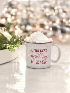 a mug with whipped cream in it sitting on a table next to a christmas tree