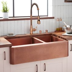 a copper sink in a kitchen with white cabinets