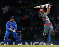 a cricket player hitting the ball with his bat while another man watches from behind him