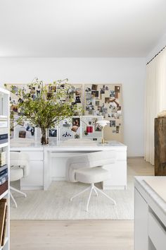 an office with white furniture and lots of pictures on the wall behind it, along with a plant