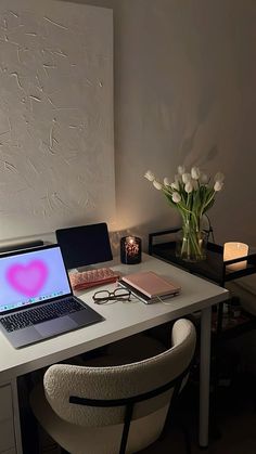 a laptop computer sitting on top of a white desk next to a vase with flowers