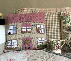 a crocheted pillow with a house on it next to two coffee mugs