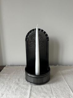 a white candle is sitting on top of a black holder that holds it in place