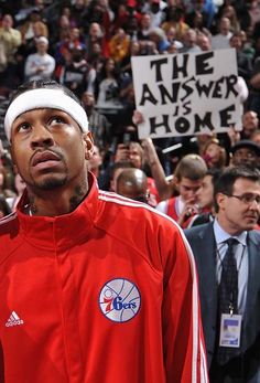 a man in a red jacket and white hat holding up a sign with the word, the answer is home