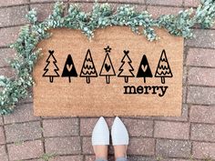 a person standing in front of a door mat that says merry with trees on it