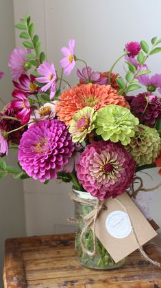 a vase filled with lots of colorful flowers on top of a wooden table next to a tag