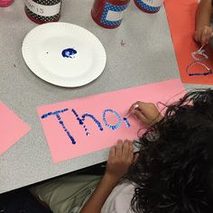 two children sitting at a table with paper plates and cups on it, making letters that spell out the word thoo