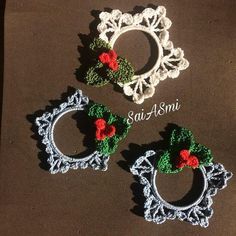 three crocheted christmas wreaths with red and green leaves on them sitting on top of a table