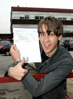 a man holding up a piece of paper in front of his face and pointing to the camera