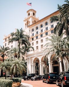 cars parked in front of a large white building with palm trees on both sides and an american flag at the top