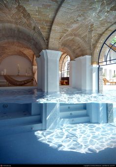 an indoor hot tub in the middle of a room with stone walls and arched windows