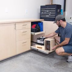 a man kneeling down in front of a cabinet filled with drawers and other items on the floor