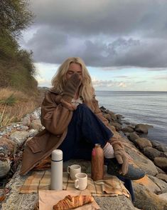 a woman is sitting on the rocks by the water holding her hands up to her face