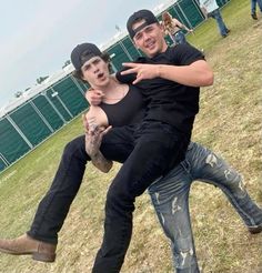 two young men sitting on top of each other in front of a fenced field