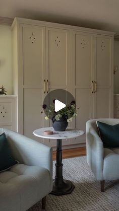 a living room with two chairs and a table in front of it, next to cupboards